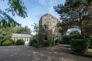 A historic stone building with a large archway, surrounded by lush greenery and a modern glass conservatory. - 2 Bed in Tunstall (oc-ivylod) (Rendlesham)