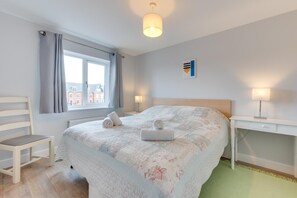A hotel room with a bed, a chair, a desk, a lamp, and a window with curtains.