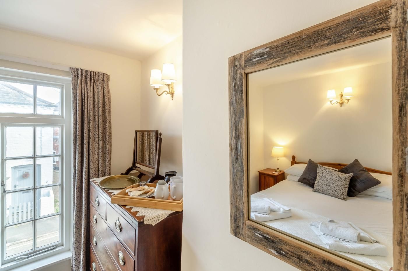 A hotel room with a bed, bedside table, lamp, and a dresser with a mirror.