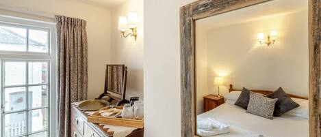 A hotel room with a bed, bedside table, lamp, and a dresser with a mirror.