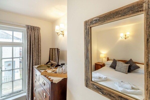 A hotel room with a bed, bedside table, lamp, and a dresser with a mirror.