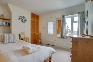 Une chambre à coucher comprenant un lit, une armoire en bois, une chaise, un bureau avec une lampe et une fenêtre avec des rideaux.
