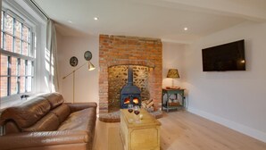 Ein Wohnzimmer mit Kamin aus Backsteinen, einer Ledersofa, einem Holztisch und einem Fernseher an der Wand.