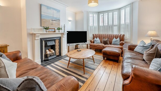 Ein Wohnzimmer mit Kamin, Ledersofas, Fernseher und einem großen Fenster mit Rollläden.
