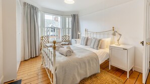 Ein Schlafzimmer mit einem großen Bett, einem Nachttisch mit Lampe und Blick auf Gebäude durch das Fenster.