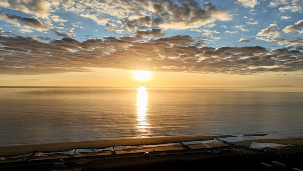 Um pôr do sol sobre um mar calmo, com um cais que se estende na água.