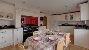 Une cuisine moderne avec des meubles blancs, un plan de travail carrelé de couleur rouge et une table à manger pour six personnes, recouverte d’une nappe à carreaux.
