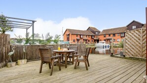 Eine Holzterrasse mit Tisch und Stühlen, ein Holzzaun und eine Reihe von Häusern im Hintergrund.