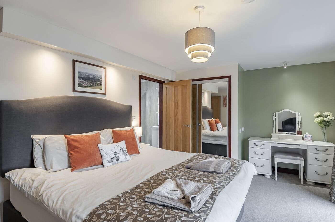 A neatly arranged bedroom with a bed, bedside tables, a desk, and a mirror.