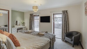 Ein Schlafzimmer mit Bett, Schreibtisch, Stuhl, Fernseher und einer Schiebetür zu einem Außenbereich.