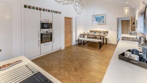 Een moderne keuken met witte kastjes, een inbouwoven en een eethoek met een bank.