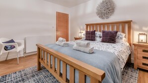 Een slaapkamer met een houten bed, een witte stoel, een nachtkastje met een lamp en een decoratief object aan de muur.