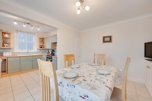 A compact kitchen with a dining area, featuring a table set for four, a television, and a small window. - 2 Bed in Southwold (oc-kin) (Southwold)