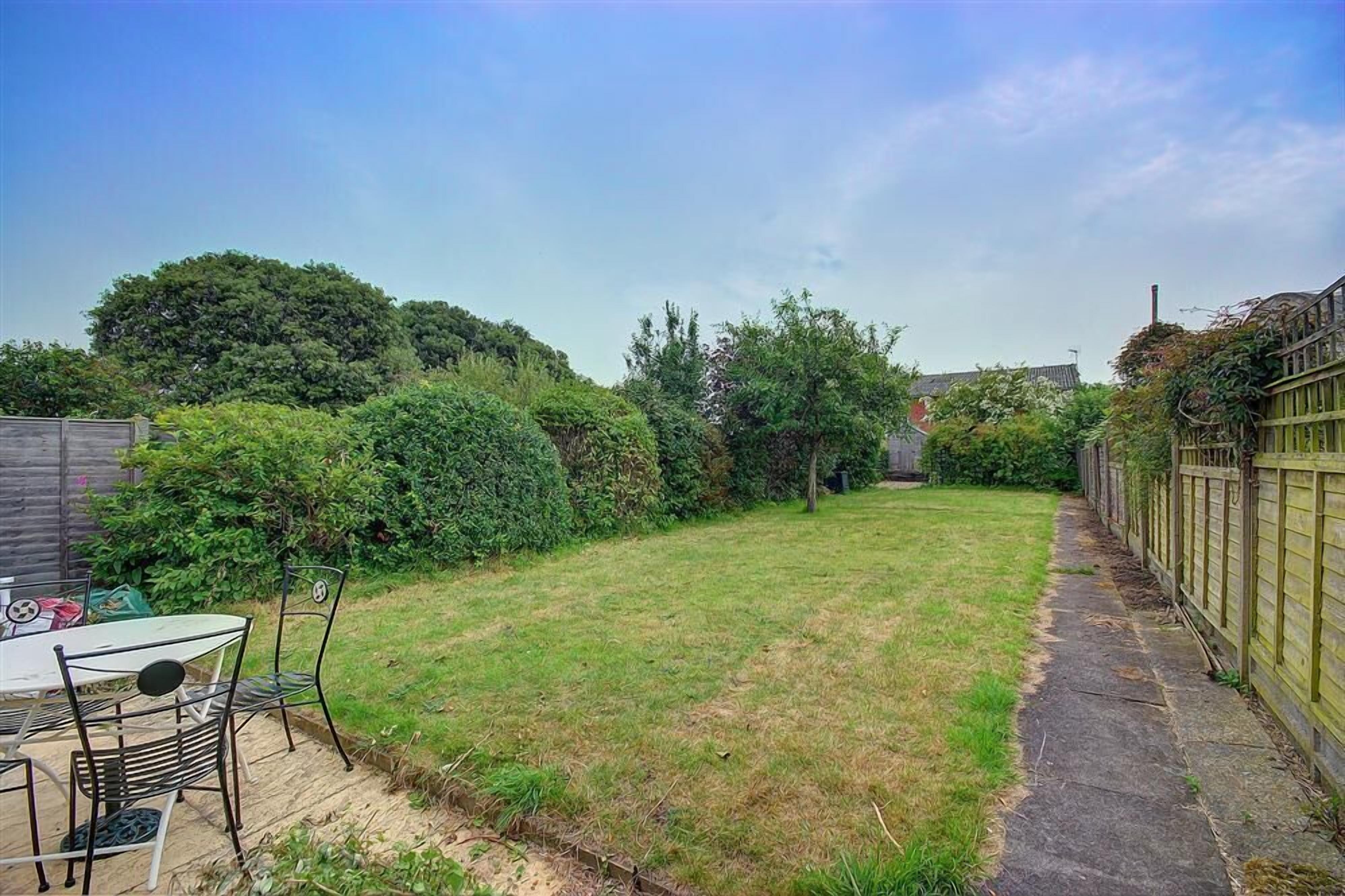 A backyard with a grassy lawn, a table with chairs, and a wooden fence.