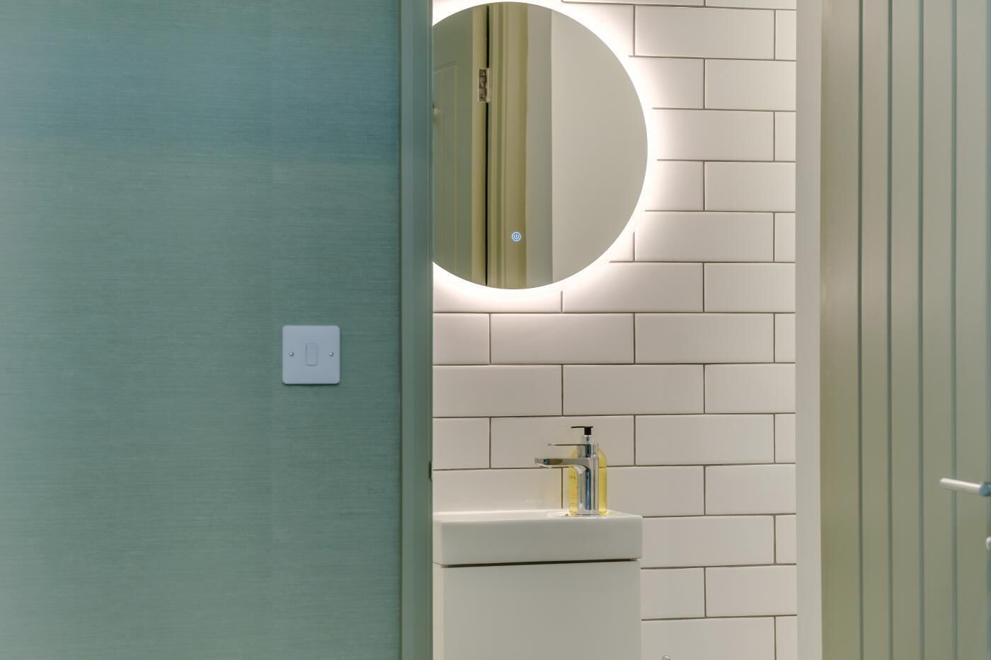 Un baño con lavamanos blanco, un espejo y una lámpara sobre el espejo.