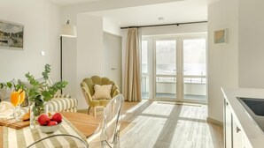 Ein modernes Wohnzimmer mit Essbereich, einem grünen Sessel und Meerblick durch große Fenster.