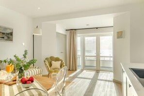 Ein modernes Wohnzimmer mit Essbereich, einem grünen Sessel und Meerblick durch große Fenster.