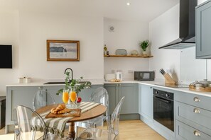 Eine moderne Küche mit Essbereich, inklusive Kücheninsel, klaren Stühlen und einem Tisch, der mit Speisen und Getränken gedeckt ist.