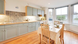 A modern kitchen with light blue cabinets, a wooden countertop, and a dining area with a table set for four. - 1 Bed in Southwold (oc-sl162) (Southwold)