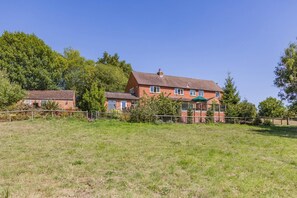 A large brick house with a green roof, surrounded by a fenced yard and trees. - 5 Bed in Clows Top (oc-m32976) (Clows Top)