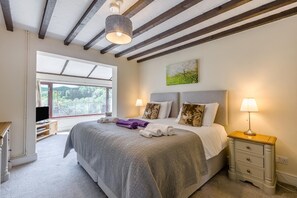 A bedroom with a large bed, a nightstand, a lamp, a painting, and a window with a view of greenery. - 5 Bed in Clows Top (oc-m32976) (Clows Top)