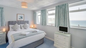 Quarto com cama, luminárias de cabeceira, televisão, cômoda e janela com cortinas.