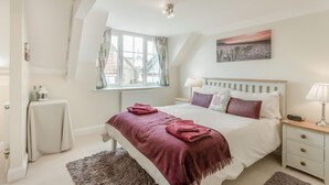 Un dormitorio con cama, mesita de noche, ventana con cortinas, radiador y un cuadro en la pared.