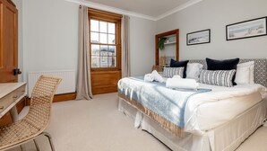 Une chambre à coucher comprenant un lit, un bureau, une chaise, une fenêtre avec des rideaux et des tableaux accrochés au mur.