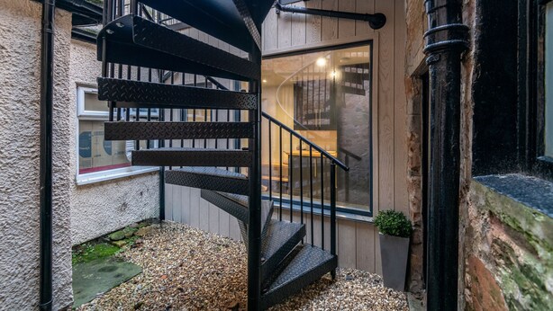 Un escalier en colimaçon avec une rampe en métal noir menant à un intérieur en bois.