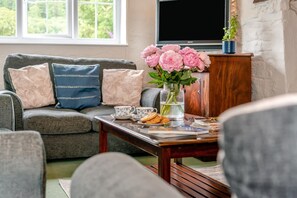 A living room with a grey sofa, a coffee table with books and a vase of flowers, and a television on a stand.