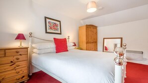 Een slaapkamer met een bed, een houten dressoir, een rode lamp, een houten garderobe, een lijstkast en een radiator.