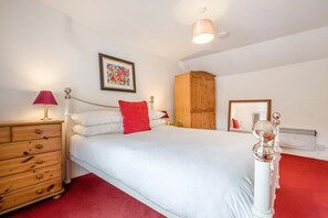 Une chambre à coucher comprenant un lit, une commode en bois, une lampe rouge, une armoire en bois, un miroir encadré et un radiateur.