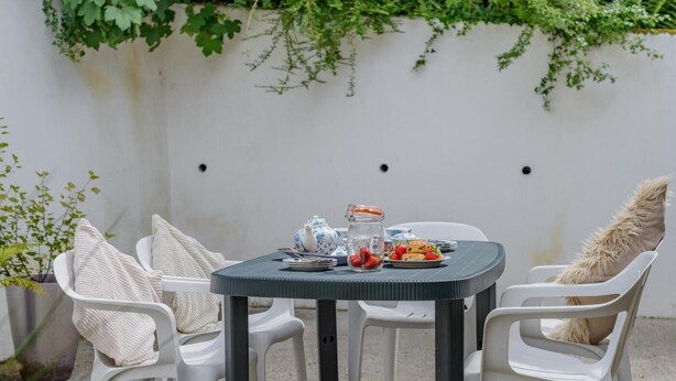 Een ronde tafel met stoelen, een theepot, een glazen pot en een bord met eten.
