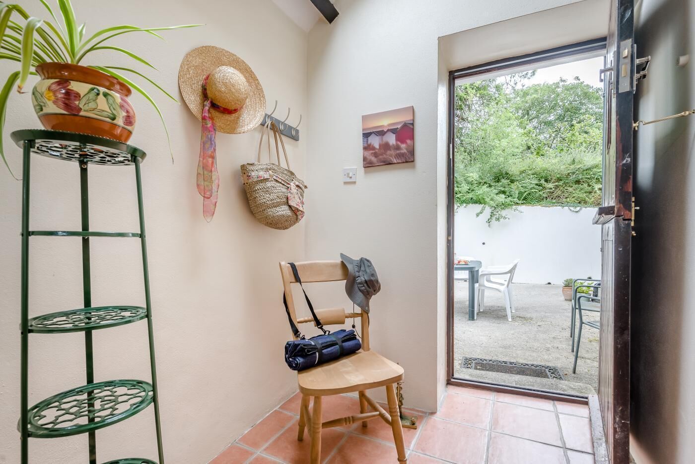 Une petite pièce avec une chaise, une plante en pot, un chapeau et un tableau accroché au mur.