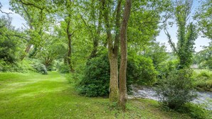 A natural landscape with a grassy area, trees, and a stream.