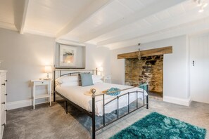 Een slaapkamer met een stenen open haard, een bed met metalen frame, een witte dressoir en een blauw vloerkleed.