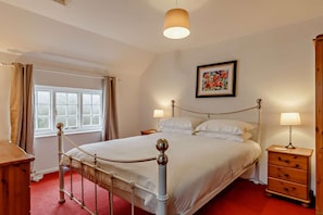 A neatly arranged bedroom with a bed, bedside tables, a window with curtains, a painting on the wall, and a chandelier.