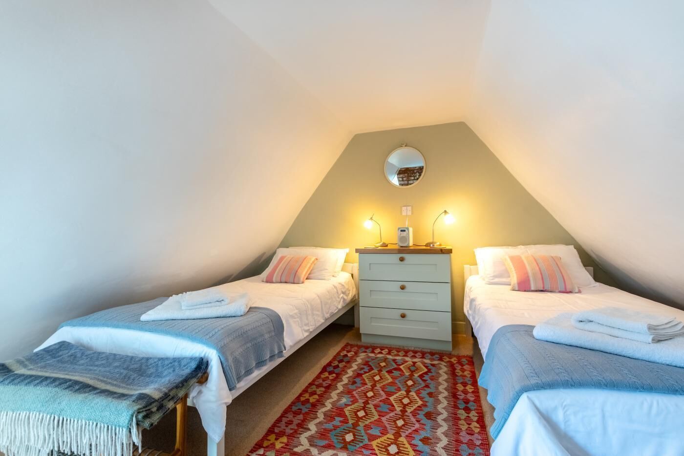 A small, cozy bedroom with two single beds, a dresser, a mirror, and a patterned rug.