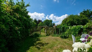 Un giardino con una pergola in legno, vegetazione lussureggiante e fiori bianchi.