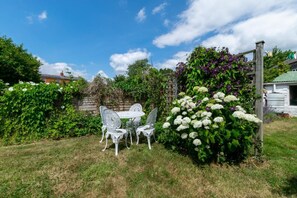 Un jardin avec une table et des chaises en métal blanc, entouré d’une végétation luxuriante et de plantes en fleurs.