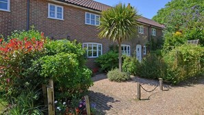A two-story brick house with a tiled roof, surrounded by a garden with various plants and a palm tree. - 2 Bed in Friston (oc-lcq) (Friston)