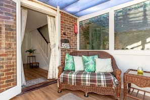A wicker sofa with a plaid blanket, a small table with a glass, and a potted plant. - 2 Bed in Friston (oc-lcq) (Friston)