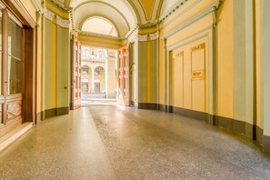 A corridor with a polished floor, wooden doors, and a view into a building with arched windows.
