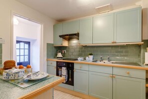 A kitchen with light green cabinets, a wooden countertop, a kettle, and a sink.