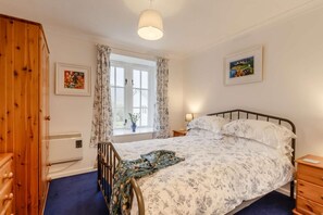 A bedroom with a bed, wooden wardrobe, window with curtains, and a nightstand with a lamp.