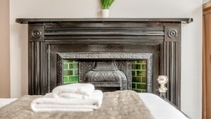 A bedroom with a fireplace, a bed with a white comforter, and a potted plant on the mantel. - 3 Bed in Southwold (oc-vth) (Southwold)