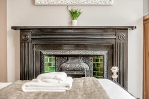 Ein Schlafzimmer mit Kamin, einem Bett mit weißer Bettdecke und einer Topfpflanze auf dem Kaminbrett.