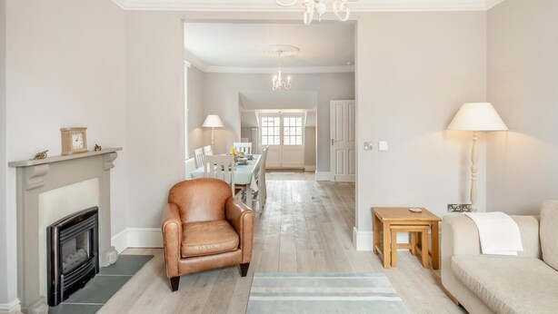 A living room with a fireplace, leather armchair, sofa, and a dining area in the background. - 3 Bed in Southwold (oc-vth) (Southwold)