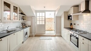 A modern kitchen with a built-in washer, a gas stove, and a large window overlooking a tiled roof. - 3 Bed in Southwold (oc-vth) (Southwold)