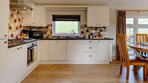 A modern kitchen with white cabinetry, a central island, a window with a view, and a dining area with a wooden table and chairs.